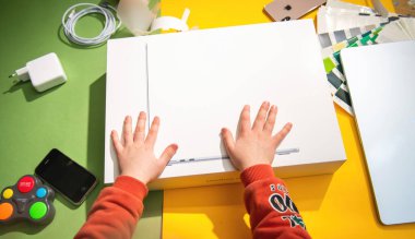 Paris, Fransa - 13 Mart 2025: Bir çocuk, teknolojik aksesuarlar ve renkli yaratıcı çalışma alanı elementleriyle çevrili bir şekilde, boks yaparken her iki elini de zevkle bir MacBook Air M4 konsept kutusuna koyar