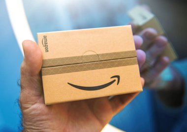 Paris, Fransa - 22 Kasım 2024: Bir insanın elinde üzerinde Amazon logosu olan küçük, kahverengi bir Amazon hediye kartı çantası var, kavisli ve aydınlatılmış bir yüzeye yansıyor..