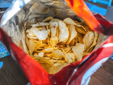 Açık bir patates cipsi torbasının içi, üst perspektiften çekilen bol miktarda çıtır çıtır altın cipsi gözler önüne seriyor..