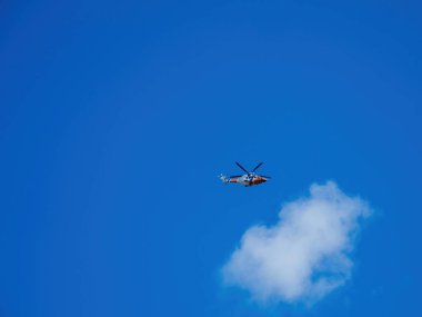 Alkmaar, Hollanda - 30 Ağustos 2024: Hollanda 'nın açık mavi gökyüzünde bir kurtarma helikopteri süzülüyor, sakin bir hava sahnesinde tek bir kabarık bulut eşliğinde.