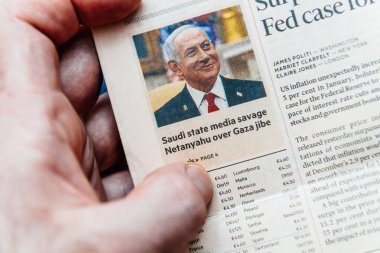 Paris, Fransa - 4 Mart 2025: Bir kişinin eli, Suudi medyasının Gazze hakkındaki yorumlarına verdiği yanıtı eleştiren başlıklı Benjamin Netanyahu 'nun yer aldığı bir gazete makalesine işaret ediyor.