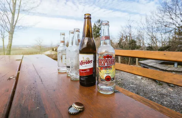 Boş bira şişeleri bir orman ortamında aşınmış ahşap bir masanın üzerinde dizilir, manzaranın manzarası arka plandadır..