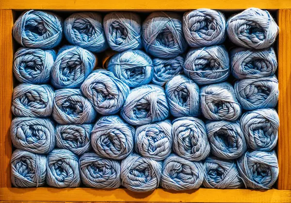 Düzenli sıralanmış mavi iplik topları ahşap bir rafı dolduruyor, çeşitli gölgeler ve el işi için dokular sergiliyor.