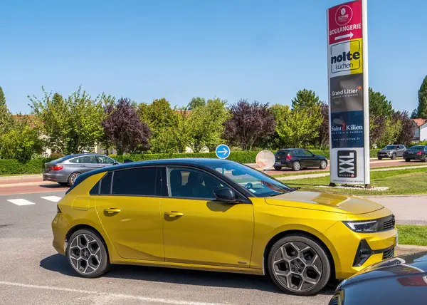 Le Touquet, Fransa - 23 Ağustos 2023: Fransa 'da Le Touquet, Fransa' da ticari bir tabela direğinin önüne park edilmiş parlak sarı bir Opel Astra, Boulangerie, Nolte Kuchen ve XXL Maison gibi çeşitli mağazaları vurguluyor..