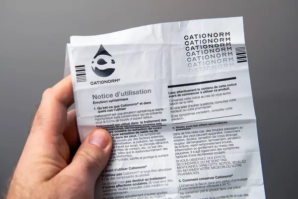 Paris, Fransa - 10 Mart 2025: Bir erkek el Cationorm oftalmik emülsiyon broşürü tutuyor Fransızca basılmış, ürün kullanımı ve yan etki bilgilerini gösteriyor, tarafsız bir arkaplanda yakından görülüyor