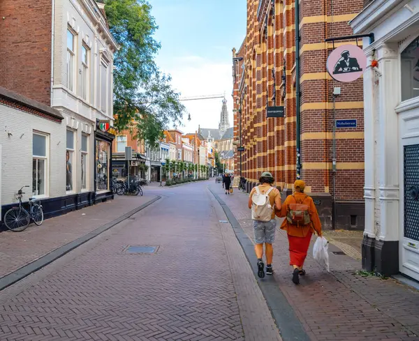 Haarlem, Hollanda - 30 Ağustos 2024: İki kişi Haarlem 'de sakin bir caddede bisikletleri ve açık bir gökyüzünün altında tarihi mimarisi ile geziniyor.