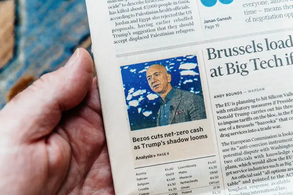 Paris, Fransa - 4 Mart 2025: Bir kişinin başparmağında Jeff Bezos ile ilgili bir makale ve politika bağlamındaki mali kesintiler başlığı yer alıyor.