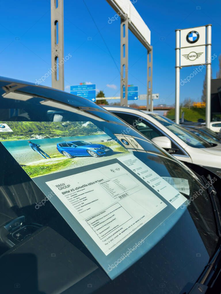 Paris, France - Mar 27, 2025: A BMW X5 xDrive50e 489ch M Sport is presented with a visible window sticker showing specifications and pricing, parked at a dealership beneath BMW and MINI branded signage