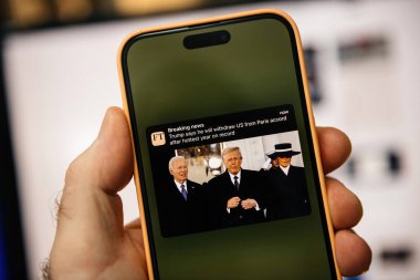 Paris, Fransa - 20 Ocak 2025: Trump 'ın, Trump, Biden ve Melania' nın görüntülerinin yer aldığı ABD 'yi Paris Anlaşması' ndan çektiğine dair bir Financial Times tebligatı yayınlayan bir iPhone elinde bulunuyor..