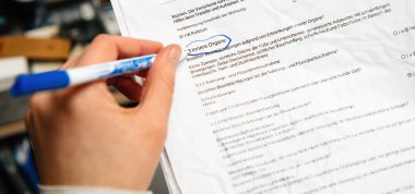 Mavi kalem tutan bir el, Innere Organe başlıklı bir bölümü işaretliyor. Yazılı bir tıbbi ankette iç organlar olarak tercüme ediliyor. Detaylı inceleme sürecini gösteriyor..