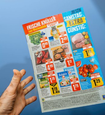 Paris, Fransa - 10 Ocak 2025: Bir el, indirimli gıda ürünleri gösteren renkli bir market ilanı tutuyor ve hafta sonu için taze ürünler ve etler de dahil olmak üzere teklifler sunuyor.