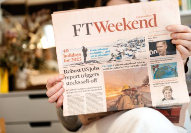 Paris, Fransa - 25 Ocak 2025: Küresel iş piyasası eğilimleri, iklim değişiklikleri ve 2025 tatilleri ile ilgili haberleri içeren FT Weekend gazetesini elinde tutan kişi.