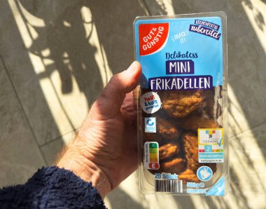 Kehl, Almanya - 14 Şubat 2025: Elinde plastik bir paket Gut ve Gunstig Delikatess Mini Frikadellen köftesi var üzerinde hazır ve sıcak ya da soğuk tüketime elverişli etiketler var.