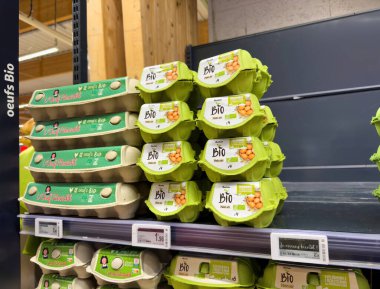 Lyon, Fransa - 14 Mart 2025: Auchan Bio ve L 'Oeuf Revestall da dahil olmak üzere Fransız markalarından gelen organik yumurta kutuları bir süpermarket rafında sırasıyla 1.96 eur ve 5.49 eur değerinde görünür fiyatlarla sergilenmektedir.