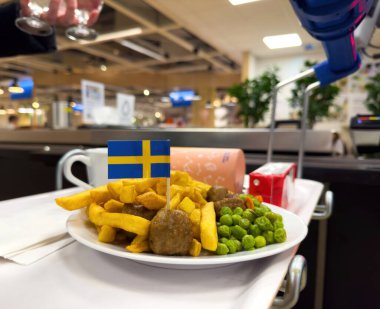 Lyon, Fransa - 15-25 yaş arası: Bir IKEA kafeteryasındaki beyaz tepside, üzerinde küçük bir İsveç bayrağı bulunan ve tipik yemek aletleri ve dekorlarıyla çevrili bir tabak İsveç köftesi ve patates kızartması servis edilir.