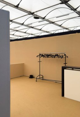 Şeffaf tavanı olan boş bir bej odada siyah elbise askıları, yerde siyah silindirik bir nesne ve en az mobilyalarla dolu bir giysi rafı görülüyor.