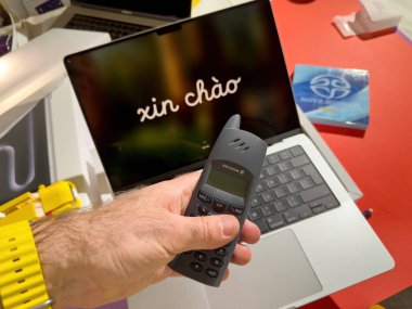 Paris, Fransa - 26 Mart 2025: Sarı saat takan bir el, renkli bir yaratıcı çalışma alanına yerleştirilmiş renkli bir hoş geldin mesajı içeren açık bir MacBook Pro M4 Max 'in üzerinde Ericsson DECT telefonu tutar.