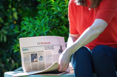 Paris, Fransa - 9 Nisan 2025: Güneşli bir bahçede FT Weekend okuyan bir kadın, ABD borsa mücadeleleri ve Avrupa bankalarının görünür ön sayfada yer alan iklim vaatlerini kolaylaştırmasıyla ilgili manşetler attı