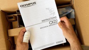 Paris, Fransa - 9 Nisan 2024: Bandajlı başparmağı olan bir kişi içinde Olimpos CX22 biyolojik mikroskobu bulunan bir karton paketi açıyor.