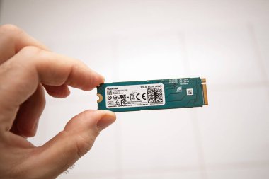 Paris, Fransa - 28 Kasım 2022: Bir el Toshiba M.2 NVMe 'nin teknik ve sertifika bilgileriyle etiketlenmiş katı devlet sürücüsünü tutuyor, küçük bir arkaplana karşı kompakt yeşil devre kartı ve altın konnektörünü vurguluyor.