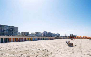 Le Touquet, Fransa - 23 Ağustos 2025: Parlak yaz güneşi, modern bina ve turistlerin yanında kıyılarda renkli kulübeler ve turuncu şemsiyelerin yer aldığı Fransa 'daki Le Touquet' nin geniş kumlu plajını yıkıyor.