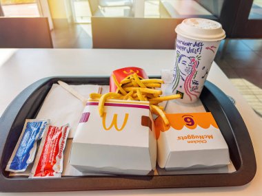 Berlin, Almanya - 14 Eylül 2023: Bir McDonald tepsisi hamburger, tavuk nugget, patates kızartması, ketçap paketleri, peçeteler ve resimli kahve fincanı bir restoran masasında duruyor