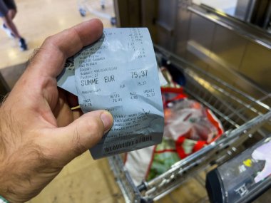 Berlin, GErmany - Sep 14, 2023: Parlak ışıklı bir dükkanda poşetlerle dolu bir alışveriş arabasının üzerinde toplam 75.37 Euro 'luk ayrıntılı bir Alman bakkal fişi bulunuyor