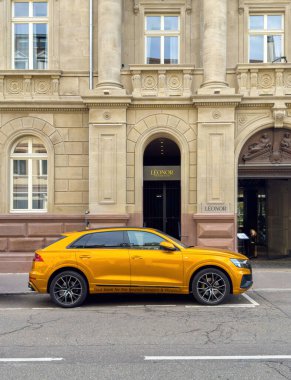 Strasbourg, Fransa - 7 Ekim 2023: Parlak sarı Audi SUV Strasbourg 'daki lüks Leonor otelinin önüne park etmiş zarif taştan frakesi, kemerli pencereleri ve büyük girişi bir sokak sahnesinde görülüyor.