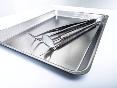 Ayna da dahil olmak üzere paslanmaz çelik diş aletleri ve steril metal tepsi üzerinde dinlenen problar parlak ışıklandırılmış klinik bir ortamda beyaz bir yüzeye yerleştirildi.