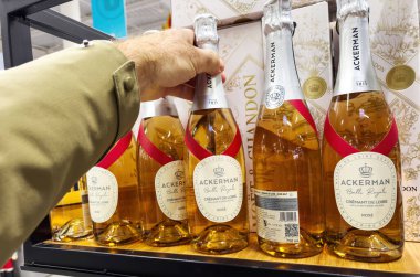 Paris, Fransa - 20 Aralık 2024: Bej ceketli bir kişi, mağaza vitrininde benzer köpüklü şarap şişeleriyle dolu bir raftan Ackerman Bulle Royale de Loire Rose şişesi seçiyor