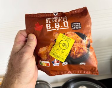 Paris, Fransa - 23 Aralık 2024: Bir erkeğin elinde bir paket BBQ tavuk kanadı sergileniyor, indirimli 45 puanlık satış ve sıcak ya da soğuk yeme seçenekleri vurgulanıyor.