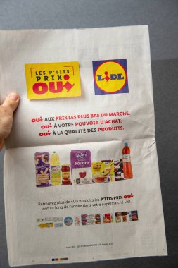 Paris, France - Mar 10, 2025: Hand holding a Lidl promotional flyer advertising the Les P tits Prix Oui campaign with featured food products, slogans highlighting low prices, and logos prominently
