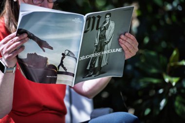 Paris, Fransa - 9 Nisan 2025: Kırmızı tişörtlü ve akıllı bir kişi açık havada bir moda dergisi okuyor, lüks Herm 'ler ve DELICATESSE MASCULINE manşetinin yer aldığı bir yayılıma açık tutuyor.