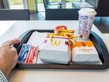 Berlin, Almanya - 14 Şubat 2023: McDonald kızartmaları, Tavuk McNuggets, soslar ve parlak bir pencerenin yanına konmuş renkli bir tasarımın yer aldığı bir bardak sodayla dolu bir masada fast food tepsisi