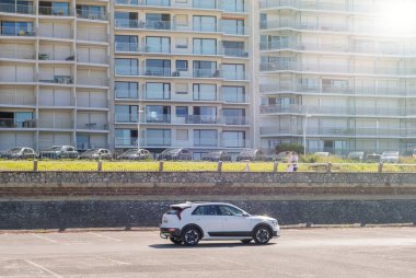 Le Touquet, Fransa - 23 Ağustos 2023: Açık bir alana park edilmiş gümüş renkli bir SUV, güneşli bir günde Le Touquet 'de deniz kenarındaki bir gezinti güvertesine ve yüksek apartmanlara bakıyor.