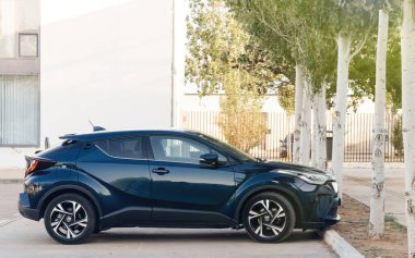Inca, İspanya - 5 Temmuz 2024: Koyu mavi bir Toyota SUV, Mallorca 'nın sessiz bir caddesinde boyalı beyaz ağaçların yanına park edilmiştir..