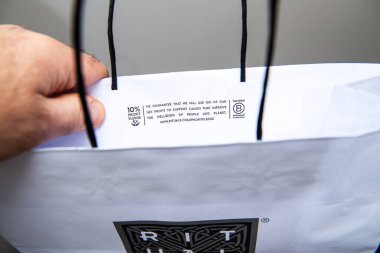 Paris, Fransa - 10 Mart 2025: Bir el, yüzde 10 kar vaadiyle ilgili bir mesaj içeren beyaz bir alışveriş torbasını tutuyor ve flep içinde sertifikalı bir B Şirketi logosu bulunuyor.
