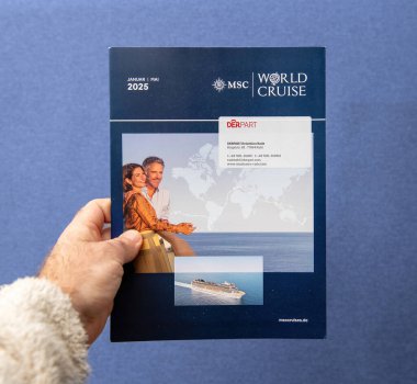 Paris, Fransa - 10 Mart 2025: Güvertede gülümseyen bir çiftin yer aldığı bir MSC Dünya Gezisi 2025 broşürü, DERPART ajansı etiketi ve kapağında yolcu gemisi resmi bulunan bir el ele tutuşma