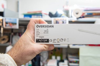 Paris, Fransa - 10 Mart 2025: Bir el, güç, parlaklık, renk sıcaklığı ve arkaplandaki karmaşaya karşı ışın açısı gibi ürün özelliklerini gösteren bir IKEA OVERSIDAN LED ışık kutusu tutuyor
