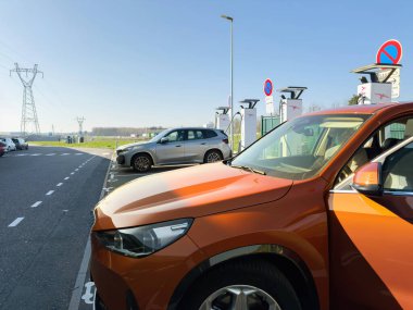 Paris, Fransa - 28 Mart 2025: Parlak turuncu bir BMW iX1 elektrikli araba açık bir günde bir yol ve açık otlak alan yakınlarındaki BMW araçlarının yanında park edilmiş ve şarj ediliyor