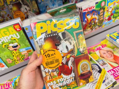 Paris, Fransa - 28 Mart 2025: Bir el Picsou Dergisi 'nin kapağında Scrooge McDuck' ın bir madeni para koleksiyonu ve bir perakende dergi vitrininde tanıtım etiketi bulunan çift katlı bir paketi tutuyor.