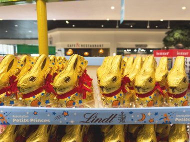 Paris, Fransa - 28 Mart 2025: Kırmızı kurdeleli ve çanları olan altın folyoyla sarılı çikolatalı tavşanlar Lindt ve Petits Prensesleriyle birlikte bir perakende mağazasında sergileniyor.