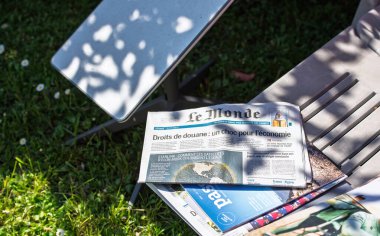 Paris, Fransa - 9 Nisan 2025: Le Monde gazetesi Starlink internet yayınını içeren bir bahçe sandalyesinde, ağaç gölgesinin altında, yeşil çimenler ve güneş ışığı altında görünen bir INternet anteni ile uzanır.