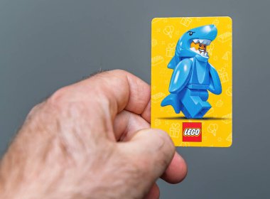 Paris, Fransa - 18 Nisan 2025: LEGO 'nun renkli bir kartının içinde küçük bir mavi köpekbalığı kostümlü, şenlik ikonları ve LEGO markalarıyla süslenmiş parlak sarı arka planda bir figürün olduğu yakın plan çekimi