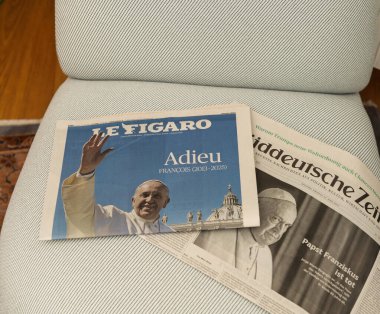 Paris, Fransa - 22 Nisan 2025: Papa Francis vergileri, Le Figaro ve Suddeutsche Zeitung 'un yer aldığı iki gazete, kısmi örtüşme ve açık manşetlerle döşenmiş bir koltukta yan yana dinleniyor.