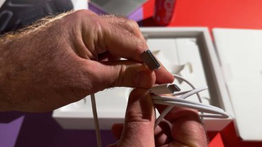 Paris, Fransa - 4 Nisan 2025: Yeni örülmüş bir Apple MagSafe kablosunu arka planda kırmızı Coca-Cola kutusu ve görünür aksesuarları olan MacBook Pro paketleme tepsisinin üzerinde tutan bir kişi