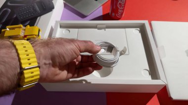 Paris, Fransa - 4 Nisan 2025: Yeni örülmüş bir Apple MagSafe kablosunu arka planda kırmızı Coca-Cola kutusu ve görünür aksesuarları olan MacBook Pro paketleme tepsisinin üzerinde tutan bir kişi