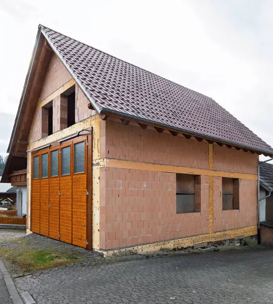 Kısmen inşa edilmiş tuğla bir garaj ya da bir Alman köyünde fayanslı çatı ve ahşap garaj kapıları olan, bulutlu bir gökyüzünün altında asfalt bir cadde boyunca kurulmuş bir ek bina.