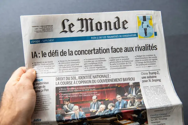 Paris, Fransa - 10 Mart 2025: Fransız Le Monde gazetesinin 10 Şubat 2025 tarihli bir sayısını elinde tutan el, yapay zeka ve ulusal kimlik politikası tartışmaları hakkında manşetler yer alıyor.