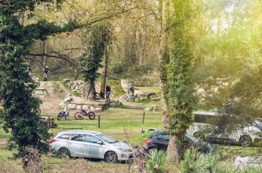 Strasbourg, Fransa - 30 Mart 2025: Ağaçlar, kayalar ve park halindeki araçlarla çevrili bir pistte pratik yapan denemeli motosiklet sürücüleriyle orman temizliği